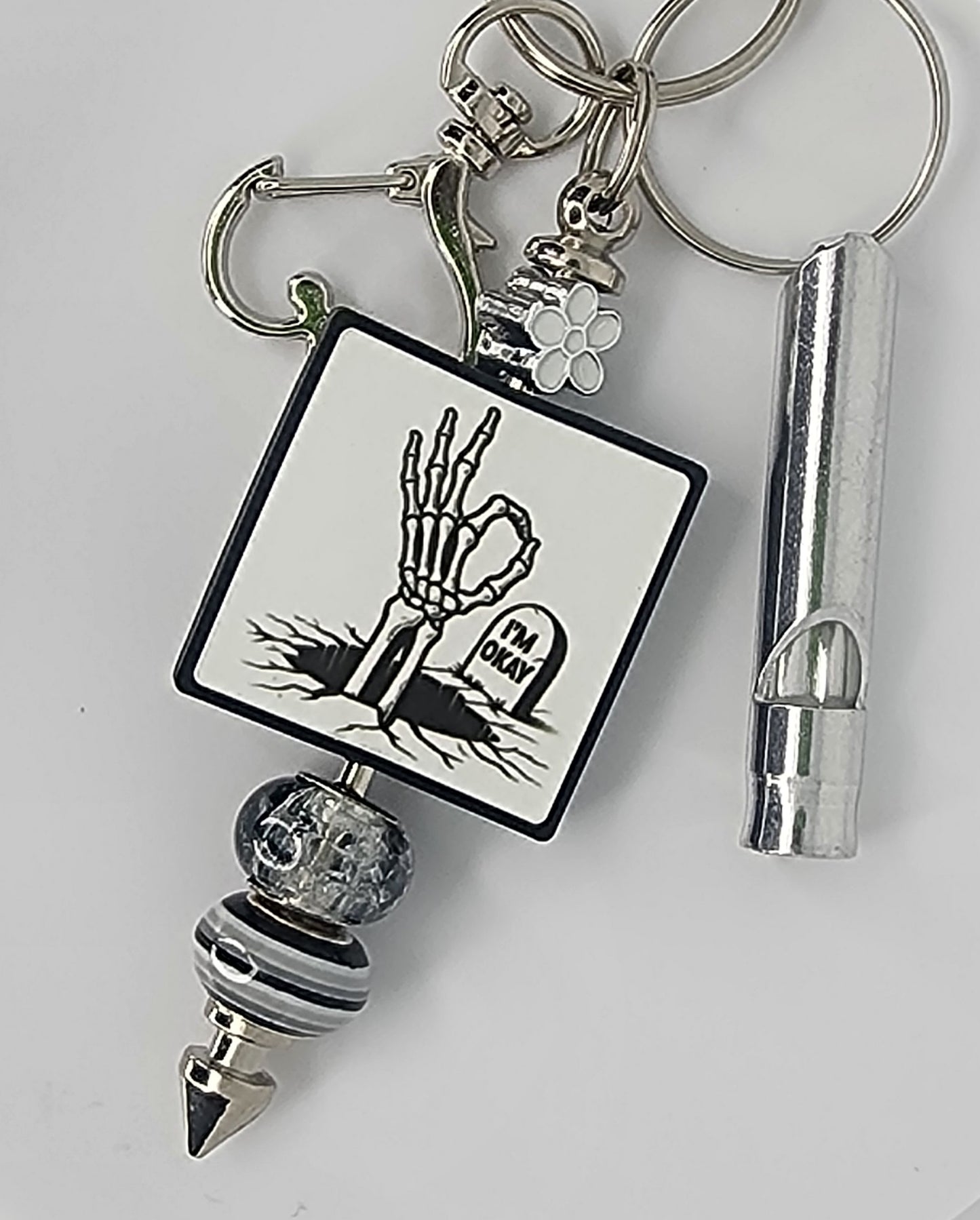 Keychain with a skeletal hand making the OK sign, with a headstone that says "I'm Okay". Also has a whistle.