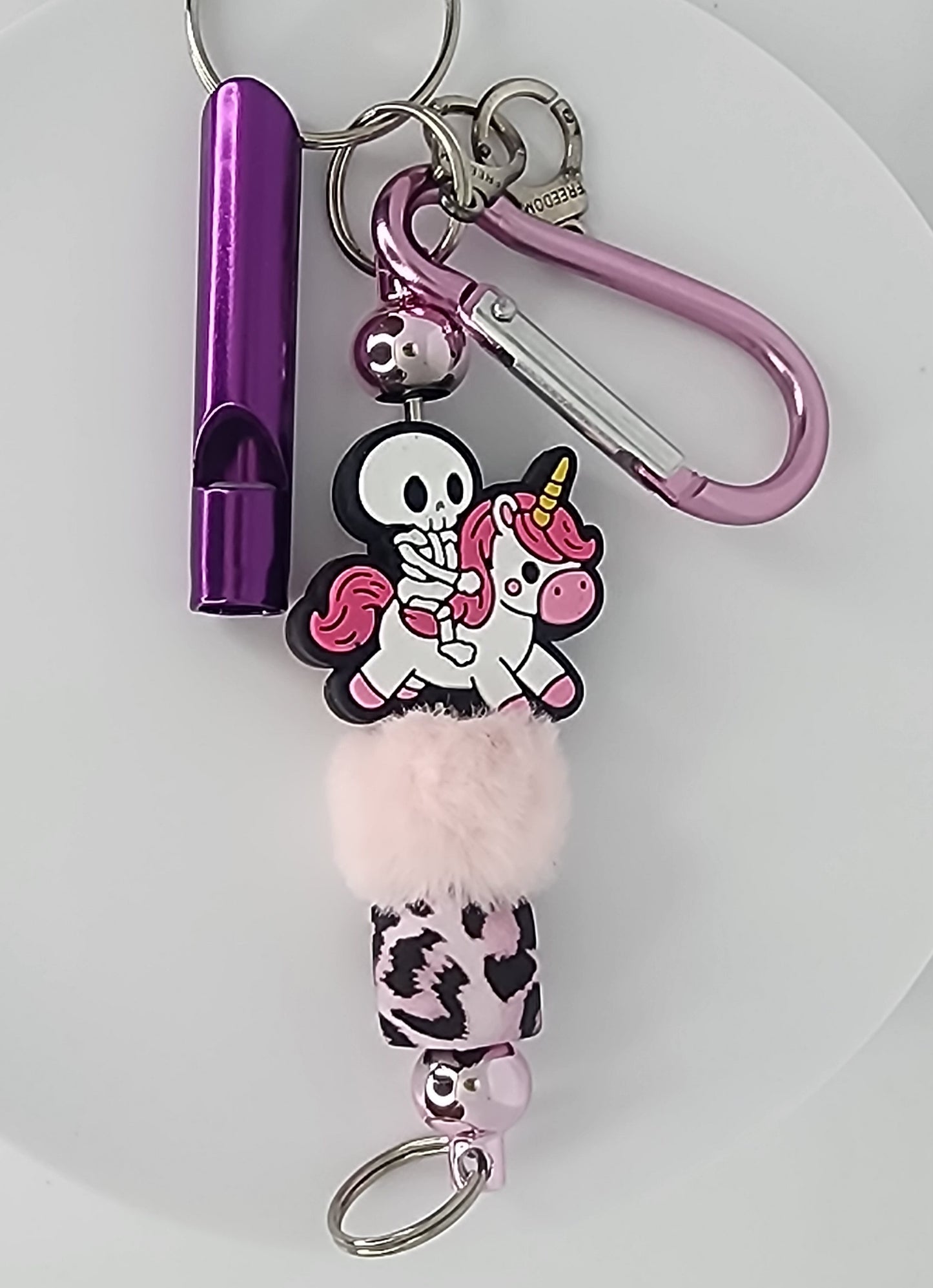 Keychain with skeleton riding a unicorn design, purple and pink colors on a white background