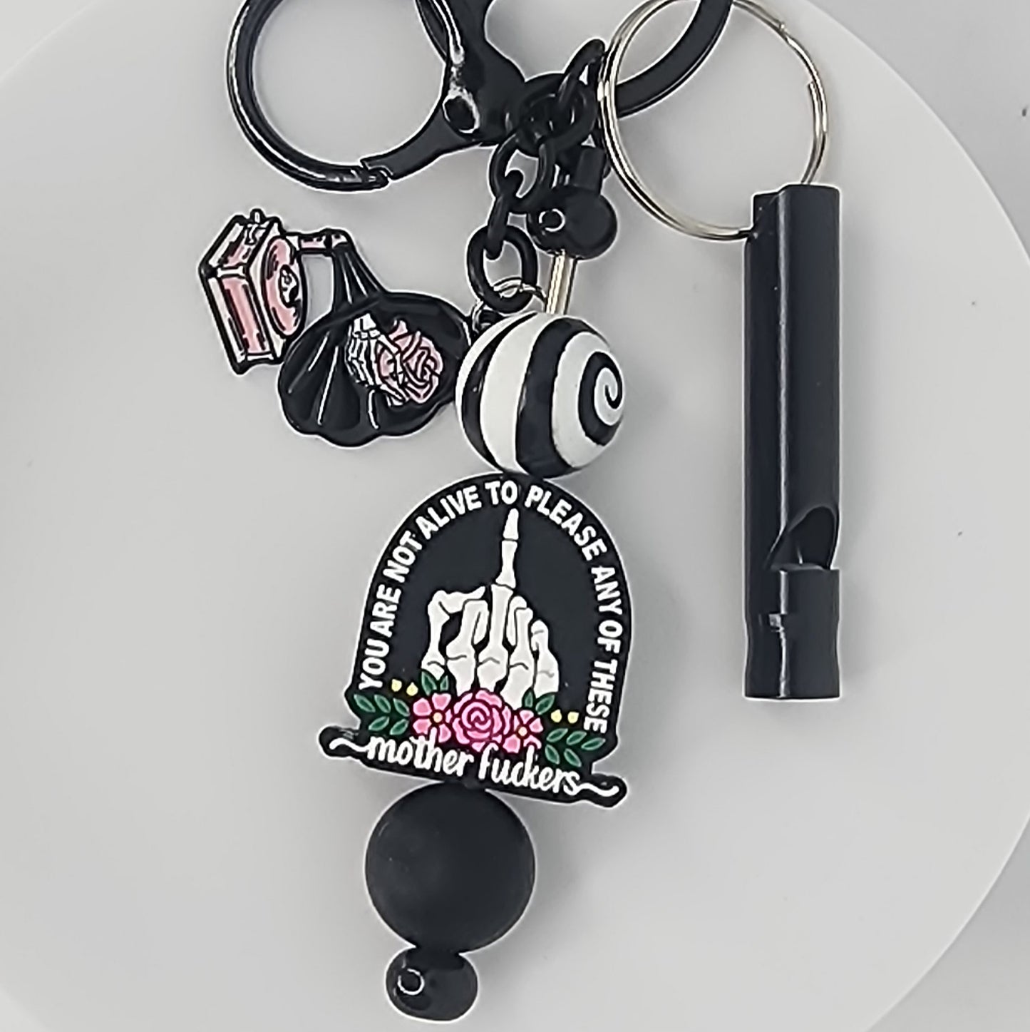 Keychain with a focal bead that says "You Are Not Alive to Please Any of These Mother Fuckers" with a skeletal hand flipping the bird on a white background.