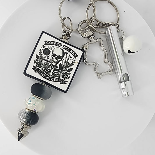 Keychain with a skeleton design that says "Coffee Makes Me Nicer," a cat-shaped clip, a white jingle bell, and a silver safety whistle.