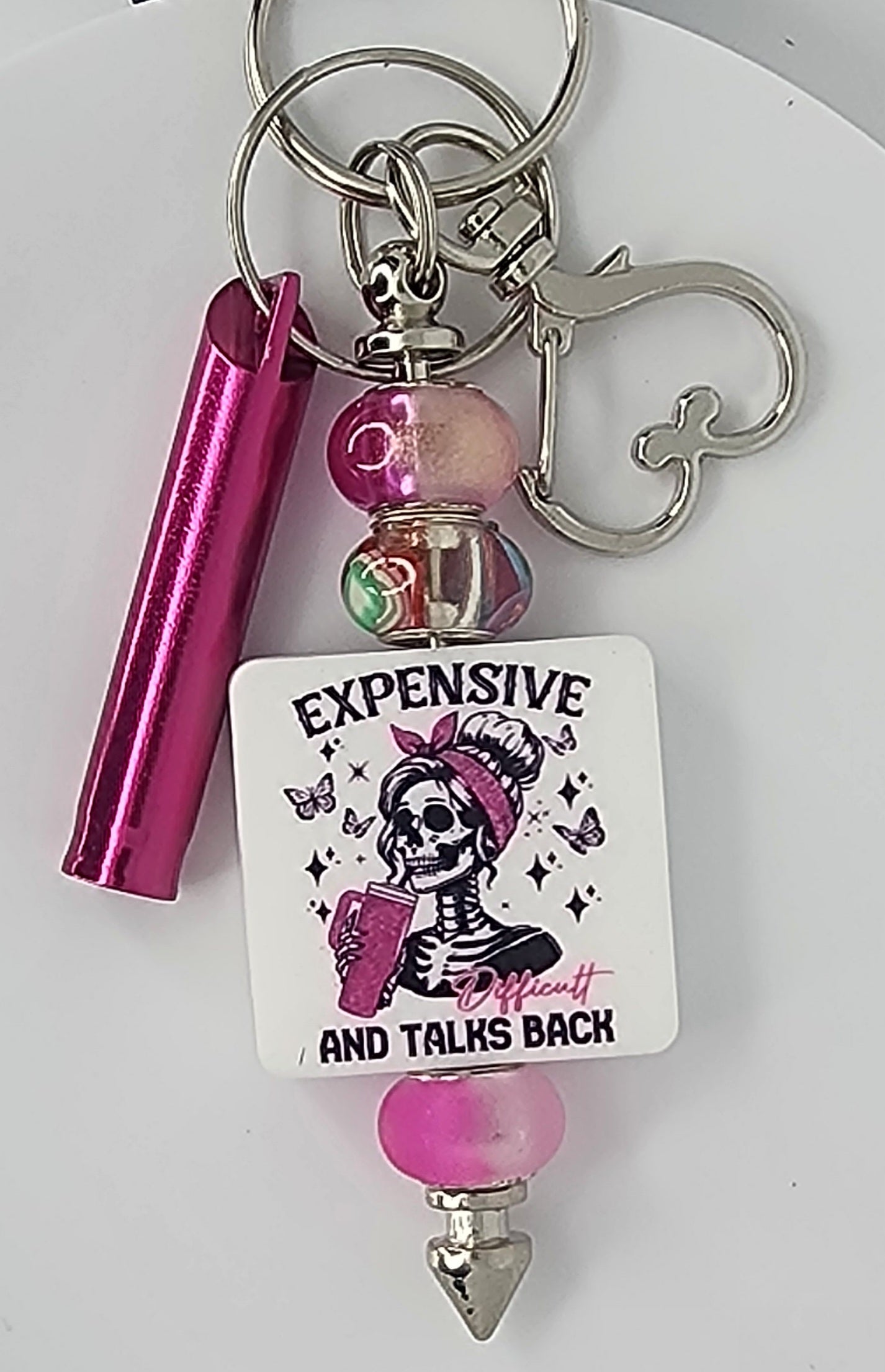 Keychain with skull design, pink accents, and text on a white background