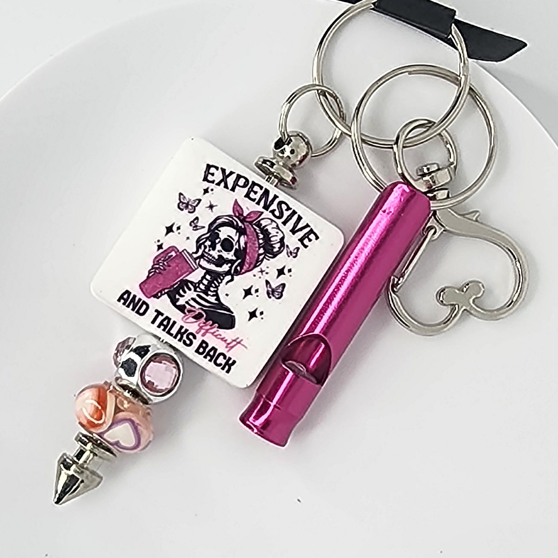 Keychain with pink whistle, skeleton design, and text on a white background