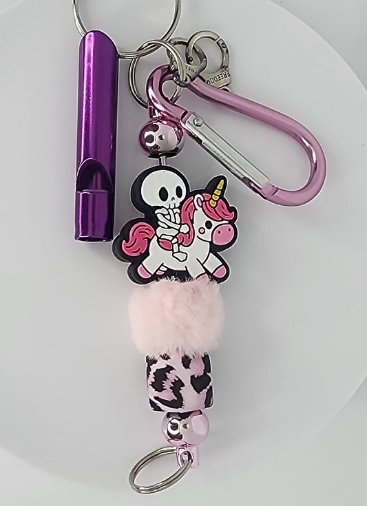 Keychain with skeleton riding a unicorn design, purple and pink colors on a white background